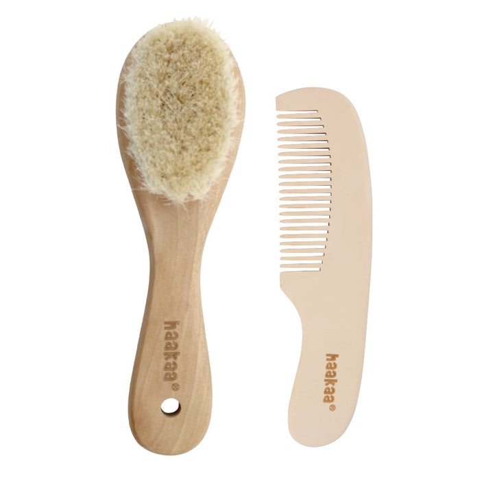 A wooden baby hairbrush with soft bristles and a matching wooden comb, both engraved with the haakaa logo, displayed side by side on a white background.