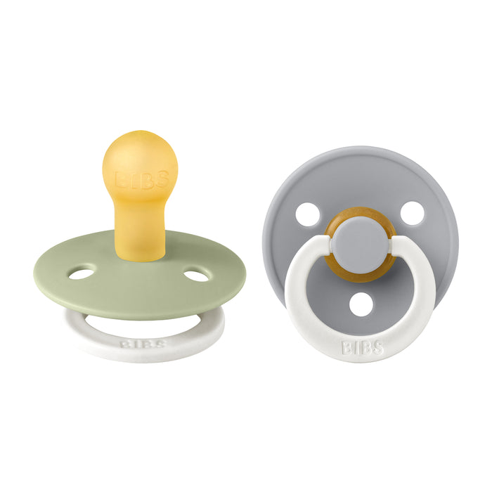 Two baby pacifiers are shown, one facing forward and one showing the back. They have soft rubber nipples, pale green and gray shields with ventilation holes, and white rings. The brand BIBS is visible on both.