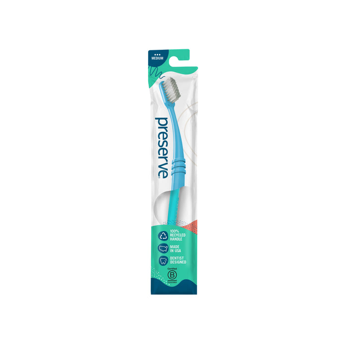 A teal Preserve toothbrush with a white bristle head is in its original packaging, labeled as made from recycled materials and BPA-free, with eco-friendly design details visible on the package.