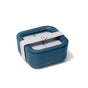 A square, blue lunch container with a transparent lid and a white, wide strap securing the lid, placed on a white background.