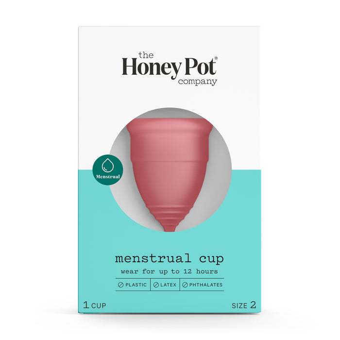 A box of The Honey Pot Company menstrual cup, visible through circular packaging cutout. The box is white and teal, labeled menstrual cup, and notes its free of plastic, latex, and phthalates. Size 2 is indicated.