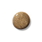 A round drop of shimmery gold glitter nail polish on a white background.