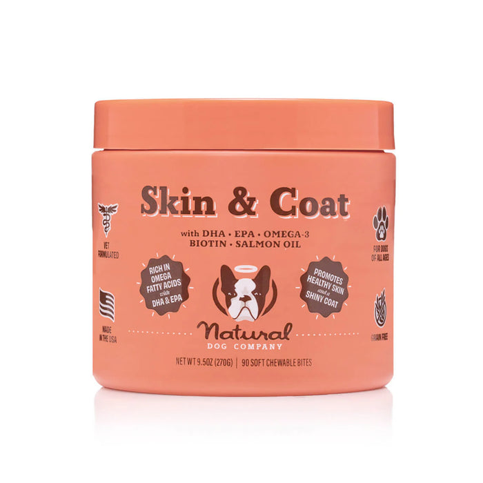 An orange container labeled Skin & Coat by Natural Dog Company, featuring DHA, EPA, Omega-3, biotin, and salmon oil, with icons and text promoting healthy skin and a shiny coat for dogs.