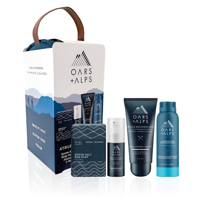 The Oars + Alps Athlete Kit comes in a white and blue box with a brown handle, featuring the mountain logo and four items: bar soap, deodorant, body wash, and recovery balm.