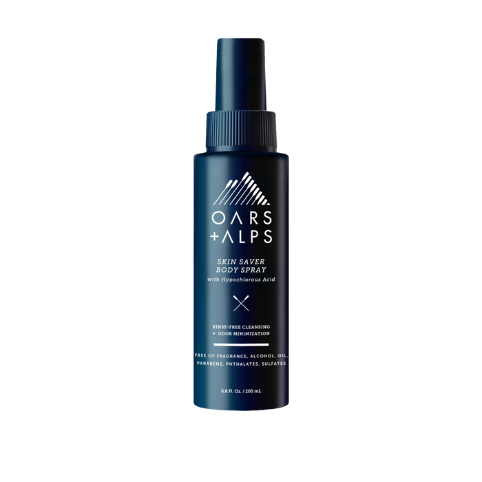 A dark blue Oars + Alps Skin Saver Body Spray bottle with a spray nozzle and white branding. The label highlights this rinse-free cleanser with hypochlorous acid is free of fragrance, alcohol, oil, parabens, phthalates, and sulfates.