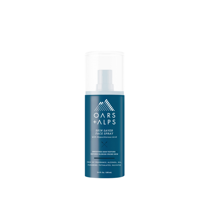 A blue bottle of Oars + Alps Skin Saver Face Spray with a white cap is shown on a plain white background. The label features key benefits in white text, including hypochlorous acid to soothe irritated skin.
