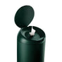 A dark green cylindrical container with a hinged lid open, showing a single wet wipe being dispensed from the center opening, set against a white background.