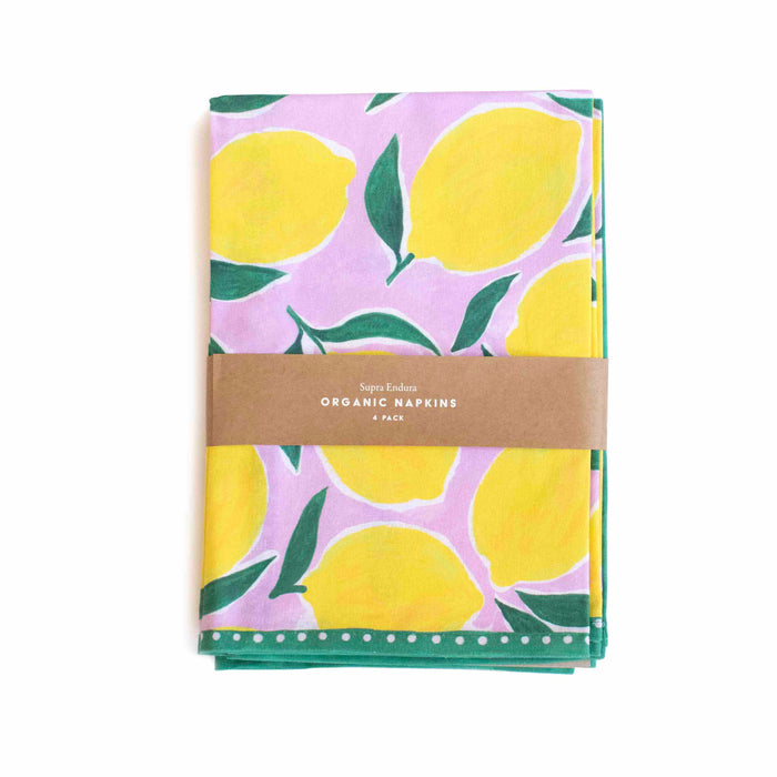 A folded cloth napkin with a pink background and bright yellow lemon and green leaf pattern, wrapped with a brown paper band labeled Organic Napkins 4 Pack.