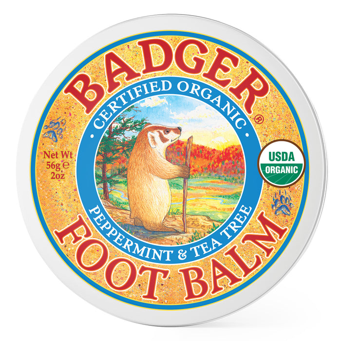 A round tin of Badger Foot Balm, labeled Certified Organic Peppermint & Tea Tree. The lid features an illustration of a badger with a walking stick in a scenic landscape. The USDA Organic seal is also visible.