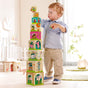 A toddler building a tall tower with HABA Stacking & Nesting Cubes - On the Farm, 12+ Months, decorated with farm animal illustrations and numbers.