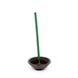 A green incense stick stands vertically in a small, round, dark brown Ceramic Incense Stick Holder by Murphys Naturals, showcasing an elegant and simple design against a pristine white background.