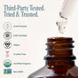 A dropper hovers above a brown Cliganic Organic Castor Oil bottle, with text and icons highlighting its features: cold-pressed, EWG verified, vegan, cruelty free, certified organic, and non-GMO. Labels emphasize third-party testing and product trust—making it an ideal choice for your Eyelash Kit or daily beauty routine.