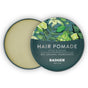 An open tin of Badger Balm Organic Hair Pomade Tin - Style & Shine reveals the pomade inside. The lid is decorated with illustrations of green leaves and citrus fruit, along with text that reads “Hair Pomade, Style & Shine, 85% Organic Ingredients.” This hair pomade offers a medium hold and uses organic beeswax for natural styling and shine.