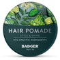A round tin of Badger Balm’s Organic Hair Pomade Tin - Style & Shine, an organic hair product adorned with botanical illustrations and text highlighting 85% organic ingredients, medium hold, style & shine, and a net weight of 56g / 2oz.