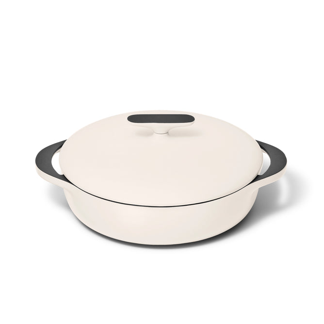 A white round Dutch oven with a matching lid and two black handles sits on a white background.