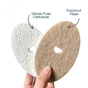 A hand holds two Scrub Be Love Oval Heart Dish Sponges (one white wood pulp cellulose, one brown coconut fiber), showing heart cut-outs; a 4-pack natural dish sponges label appears.