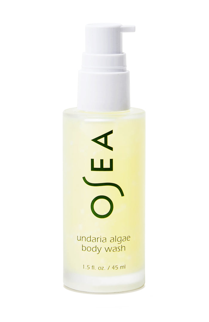 A clear bottle with a white pump dispenser containing yellow liquid, labeled OSEA undaria algae body wash, 1.5 fl. oz. / 45 ml in green text.