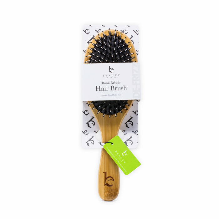 A boar bristle hair brush with a wooden handle, packaged on a white card with black text and logo. A green tag is attached to the handle, which is engraved with the brands b logo.