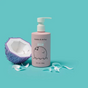 A pink pump bottle of dabble & dollop Coconut Gel stands next to a halved, stylized purple coconut on a turquoise background with white ribbon-like pieces scattered around.