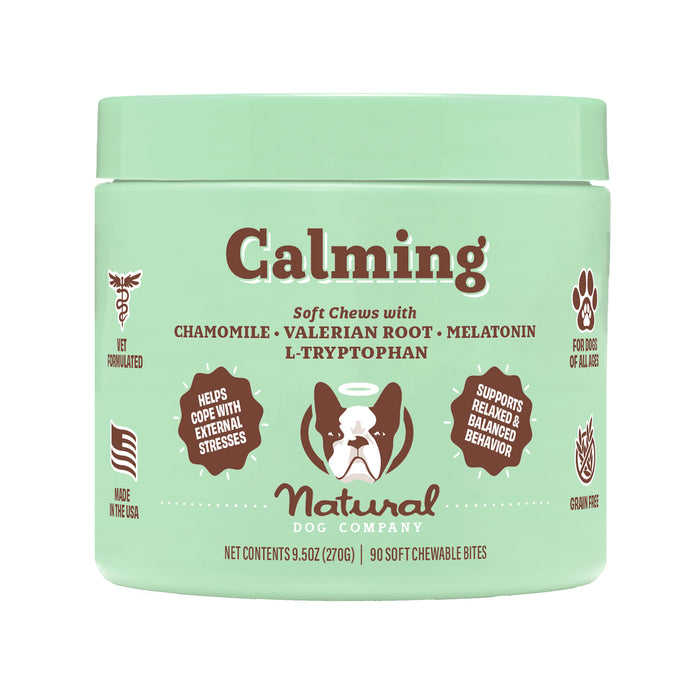 A green container of Natural Dog Company Calming Soft Chews for dogs, featuring chamomile, valerian root, and melatonin. The label highlights benefits like stress relief and balanced behavior, and icons for vet formulated and grain free.