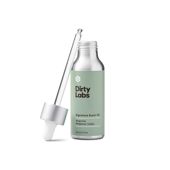 Dirty Labs Signature Scent Oil + Glass Dropper features premium Magnolia, Bergamot, and Cedar ingredients. The 50 ml (1.7 fl oz) bottle with a silver-capped dropper is elegantly designed in green and white, offering an irritant-free fragrance for a pure experience.