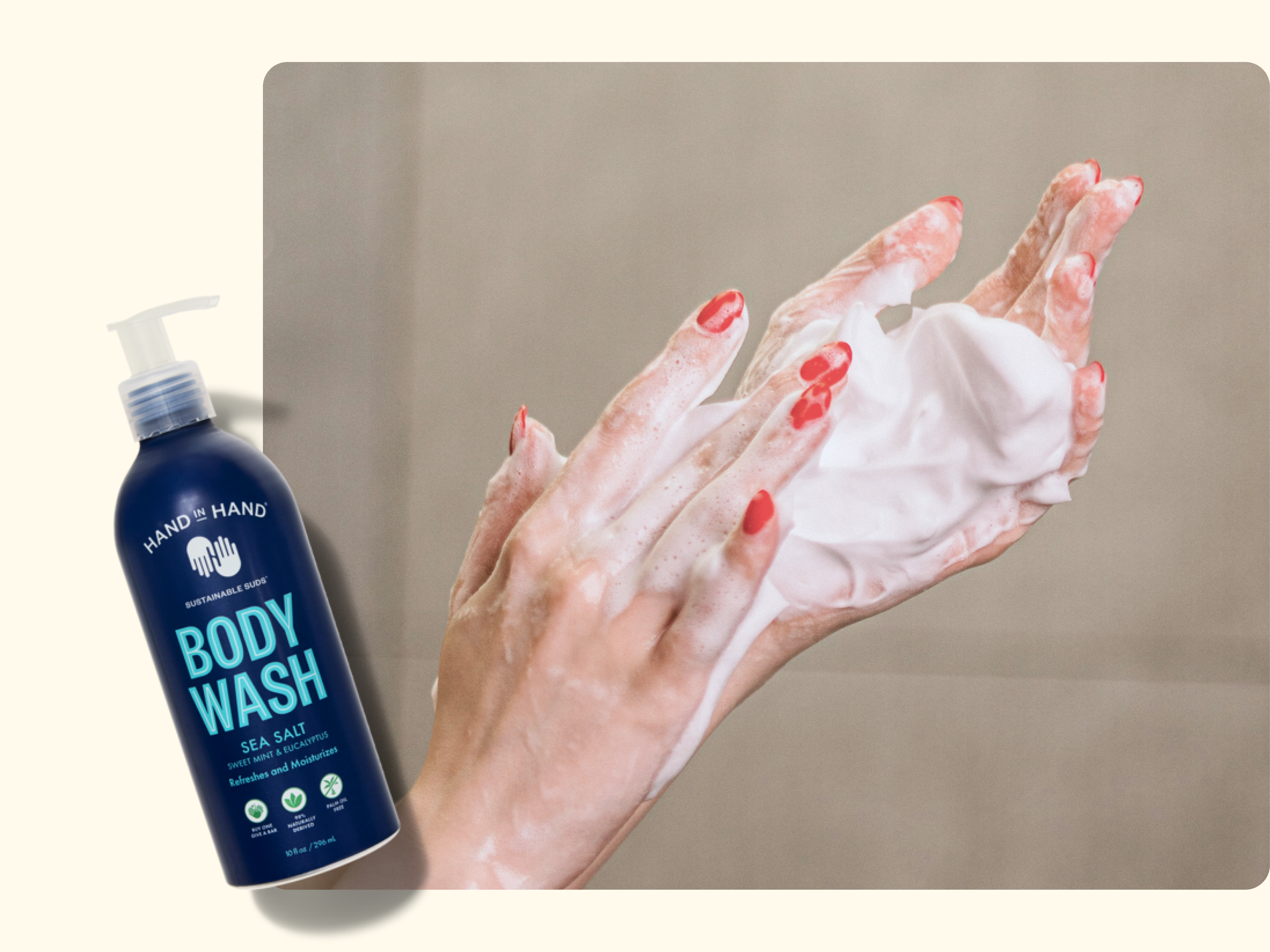 A person with red nail polish lathers their hands with foamy soap. Next to them is a blue bottle of Hand in Hand Body Wash in the Sea Salt scent with a pump dispenser.