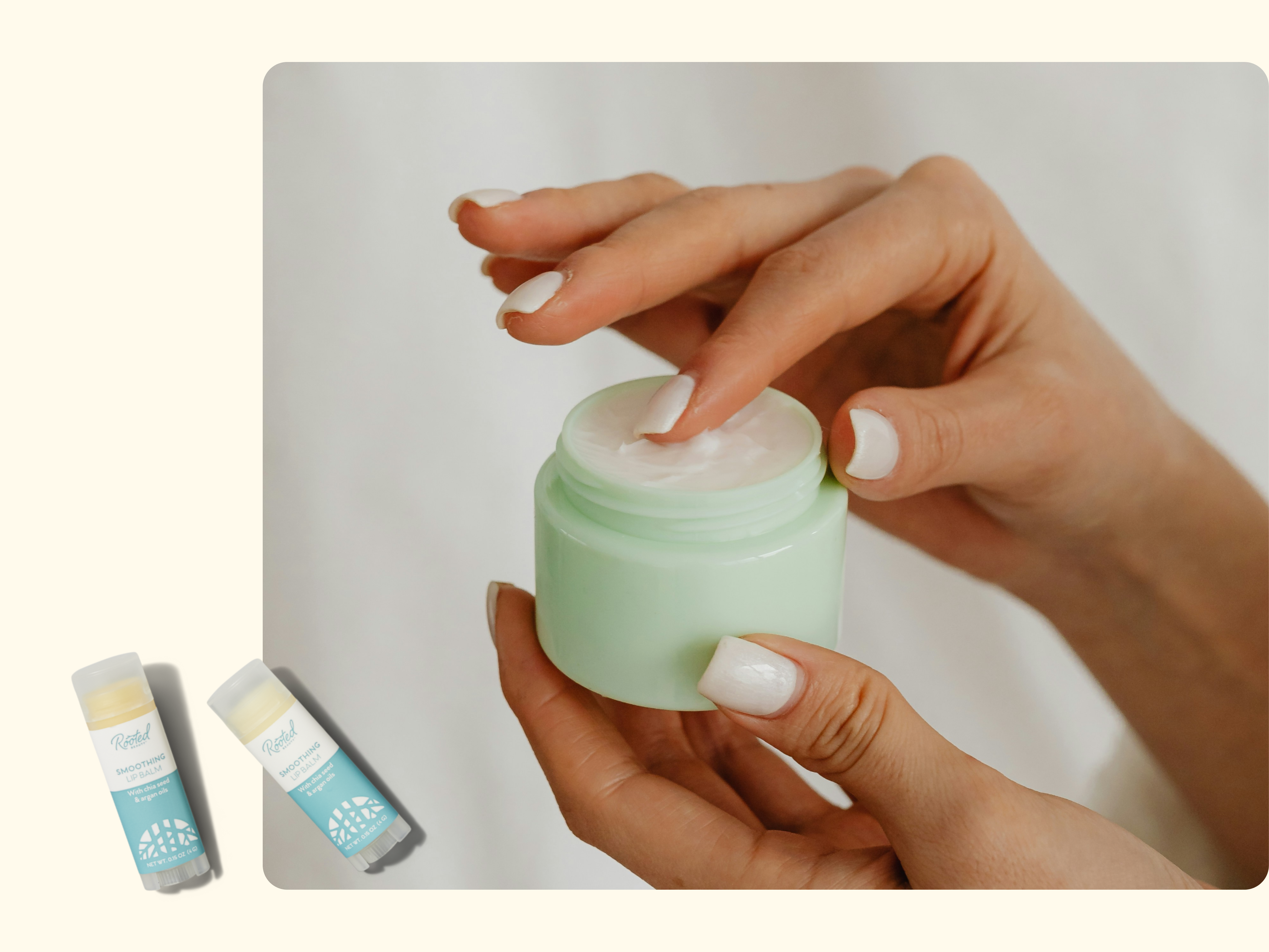 A person with neatly manicured nails dips a finger into a light green jar of cream. Two small personal care product sticks are shown on the left against a beige background.