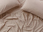 Two beige pillows and a matching Organic Crinkled Percale™ Sheet Set by Coyuchi, crafted from breathable fabric, are arranged on the bed and viewed from above. The material appears soft and comfortable, featuring natural crinkles throughout the surface.