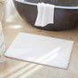 A white bath towel hangs over a modern black bathtub, and the Coyuchi Shag Organic Bath Rug is placed on a beige tile floor in a bright bathroom.