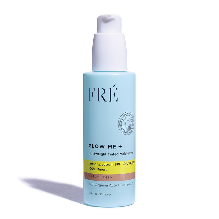 A blue bottle of FRÉ Glow Me+ Lightweight Tinted Moisturizer with a white pump dispenser. The label highlights broad spectrum SPF 30, mineral sunscreen, and Medium-Deep shade. The bottle is standing upright on a white background.