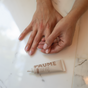 Someone applies PAUMEs All-in-One Cuticle & Nail Cream on a marble surface. Their manicured nails glow in the natural light, highlighting the nourishing blend of plant keratin and biotin that enhances both their hands smooth texture and the cream tube.