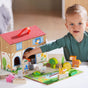 A young child smiles while playing with HABA’s Play World On the Farm, made from sustainably sourced wood for ages 18+ months, exploring animal and farmer figures, hay bales, and a colorful farm playmat.