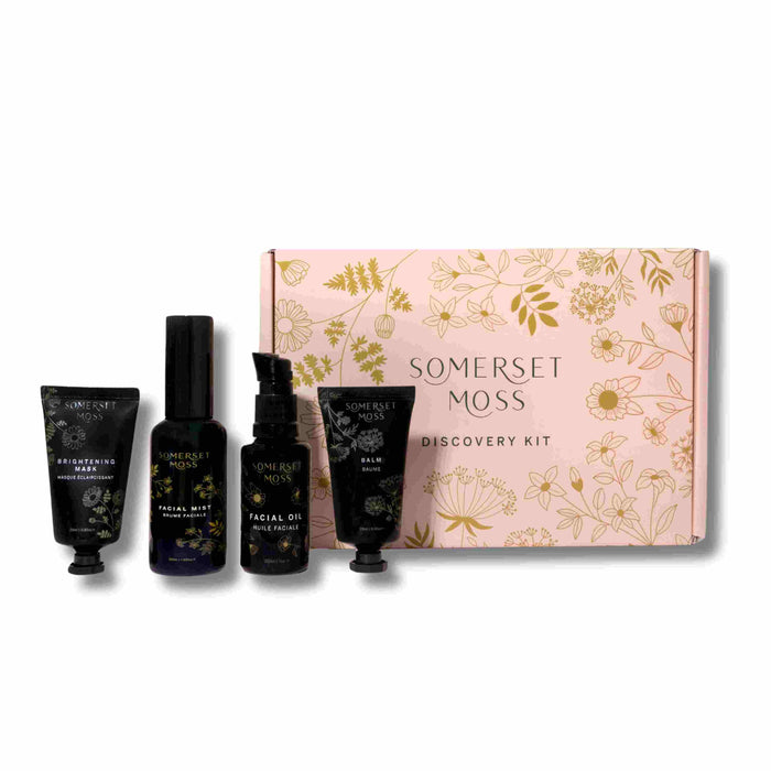 Somerset Moss Discovery Kit with four skincare products—two tubes and two bottles—arranged in front of a pink box decorated with gold floral illustrations and the brand name in gold lettering.