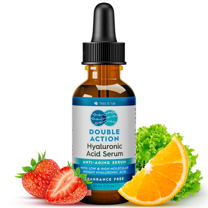 A bottle of Double Action Hyaluronic Acid Serum stands upright, surrounded by a sliced strawberry, a lettuce leaf, and a slice of orange. The label highlights anti-aging properties and that the serum is fragrance-free.