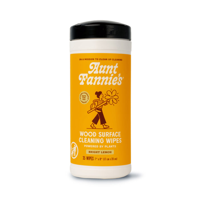A container of Aunt Fannies Wood Surface Cleaning Wipes in bright yellow packaging, labeled Bright Lemon, with an illustration of a person holding a large flower and text stating the wipes are powered by plants.