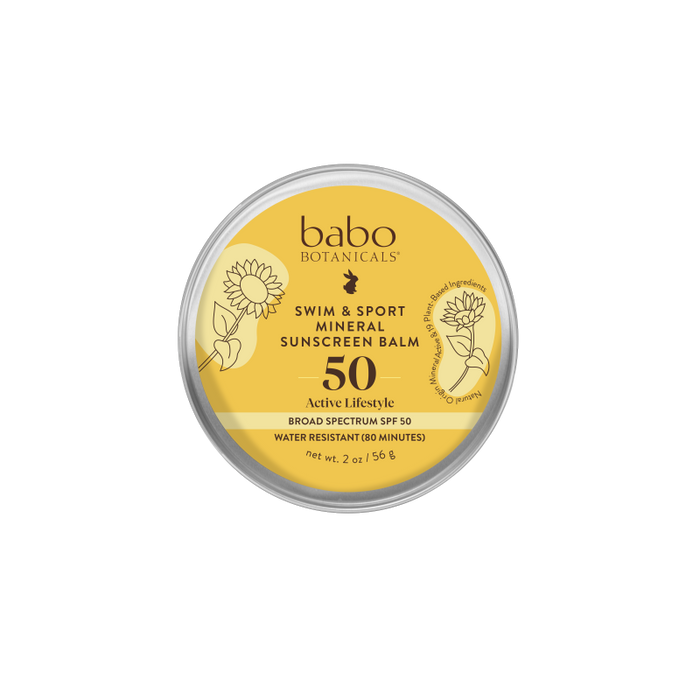 A round tin of Babo Botanicals Swim & Sport Mineral Sunscreen Balm SPF 50, featuring a yellow label with illustrations of sunflowers and product details in black text.