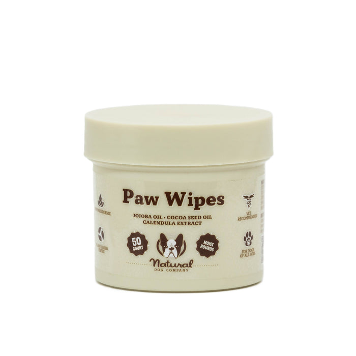 A beige container of Natural Dog Company Paw Wipes with a cream lid. The label highlights ingredients like jojoba oil, cocoa seed oil, calendula extract, and features icons for 50 wipes, and natural moisturizing.