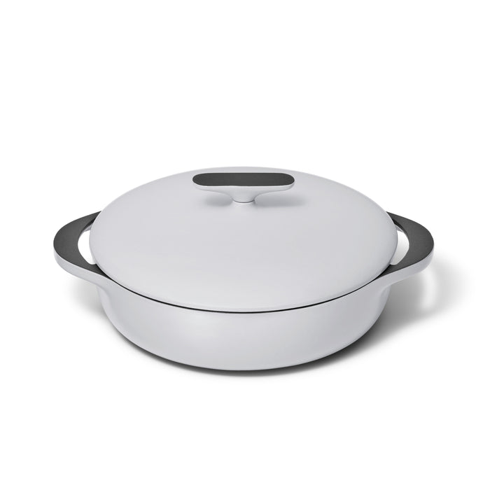 A white, round, shallow Dutch oven with a matching lid and two black handles, placed on a white background.
