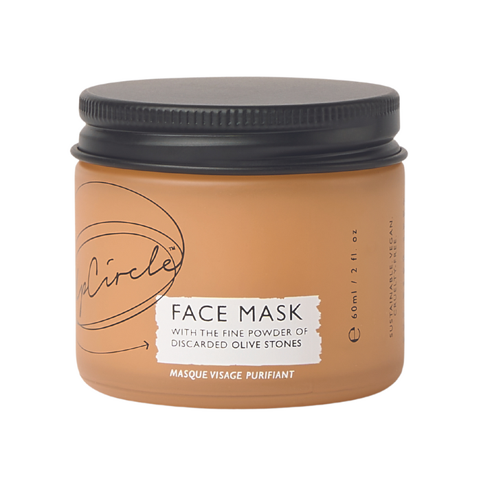 A tan jar with a black lid labeled Face Mask containing 60ml, featuring text about fine powder of discarded olive stones. The jar also says masque visage purifiant and has minimalistic design elements.