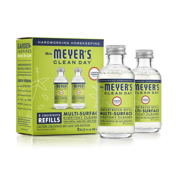 Two clear glass bottles and a green box of Mrs. Meyers Clean Day Multi-Surface Everyday Cleaner Refills, Lemon Verbena scent, are shown. The packaging highlights that it contains two concentrated refills.