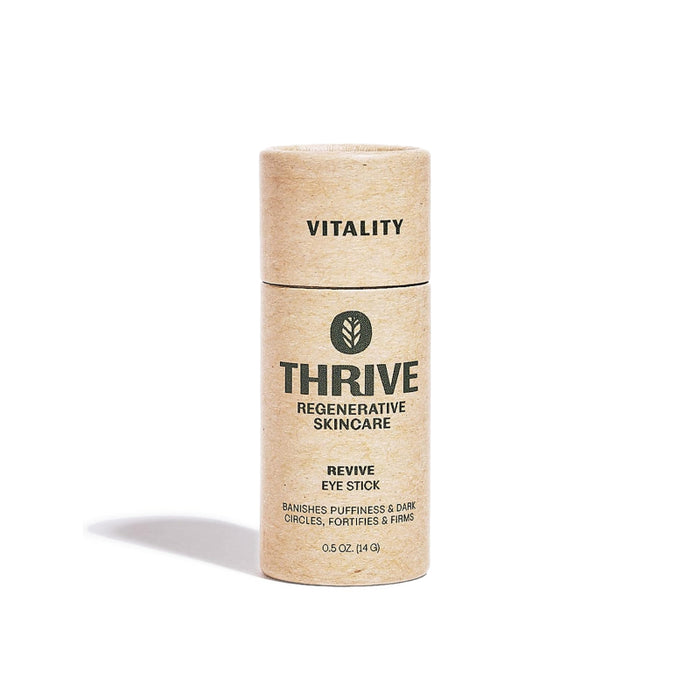 A cylindrical cardboard tube labeled THRIVE REGENERATIVE SKINCARE REVIVE EYE STICK stands upright. The packaging is natural brown with black text and a leaf logo, promoting vitality and reducing puffiness and dark circles.