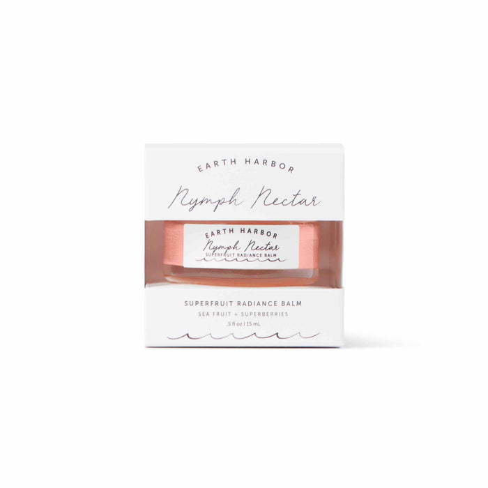 A jar of Earth Harbor Nymph Nectar Superfruit Radiance Balm in pink packaging, partially visible through a white and clear box labeled with the product name and description.
