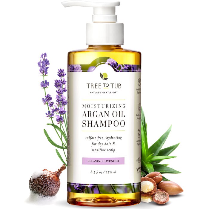 A bottle of Tree to Tub Moisturizing Argan Oil Shampoo with a pump top, surrounded by lavender flowers, argan nuts, aloe vera, and soapberries. The label notes it is sulfate free, for dry hair and sensitive scalp.