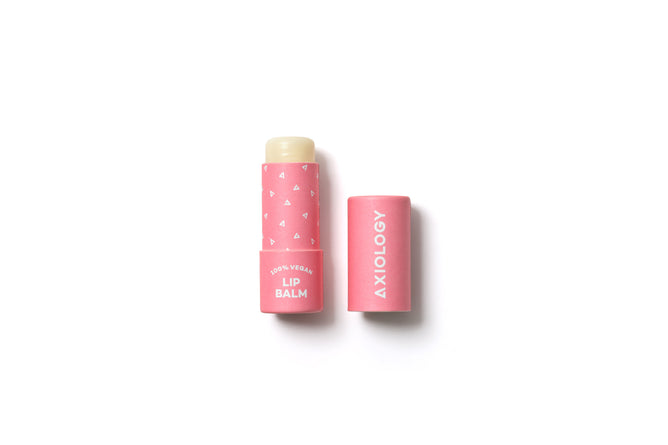 A pink tube of Axiology vegan lip balm with the cap removed and placed beside it on a white background. The tube features small white heart designs and white text.