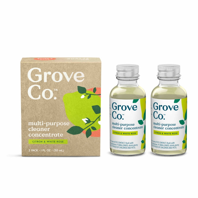 Two glass bottles of Grove Co. multi-purpose cleaner concentrate (citron & white rose) are placed next to the product’s cardboard box, which features green leaf illustrations and product information.