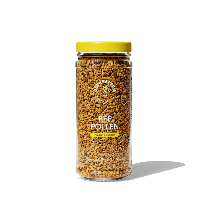 A clear glass jar with a yellow lid, filled with granulated bee pollen. The label reads Beekeepers Naturals Bee Pollen and Nourish + Support. The jar is standing on a white surface with a shadow.