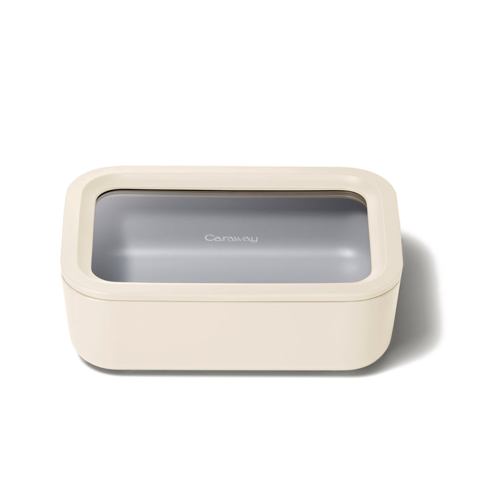 Rectangular beige food storage container with a clear, see-through lid and the word Caraway printed on top. The container is placed on a white background.