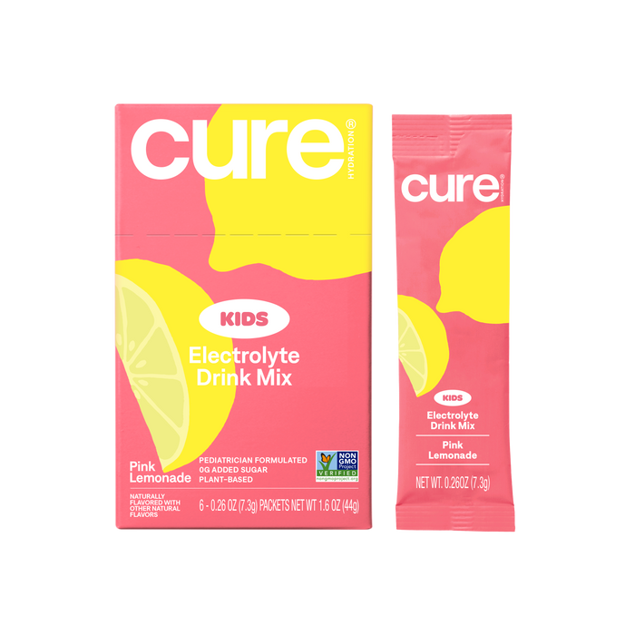 A box and a single packet of Cure Kids Electrolyte Drink Mix in Pink Lemonade flavor, featuring bright pink packaging with yellow lemon graphics and white text.