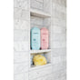 On the middle shelf of a marble-tiled shower rest two Method Body Body Wash bottles: a light blue chamomile and a pink berry. Below, a yellow shower sponge sits at the bottom.