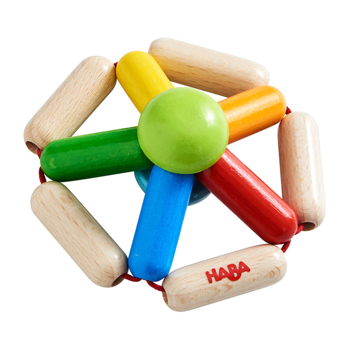 Colorful wooden baby toy with a green center and six rounded spokes in red, blue, yellow, and green, surrounded by beige wooden rods connected by red string. The brand HABA is printed on one rod.